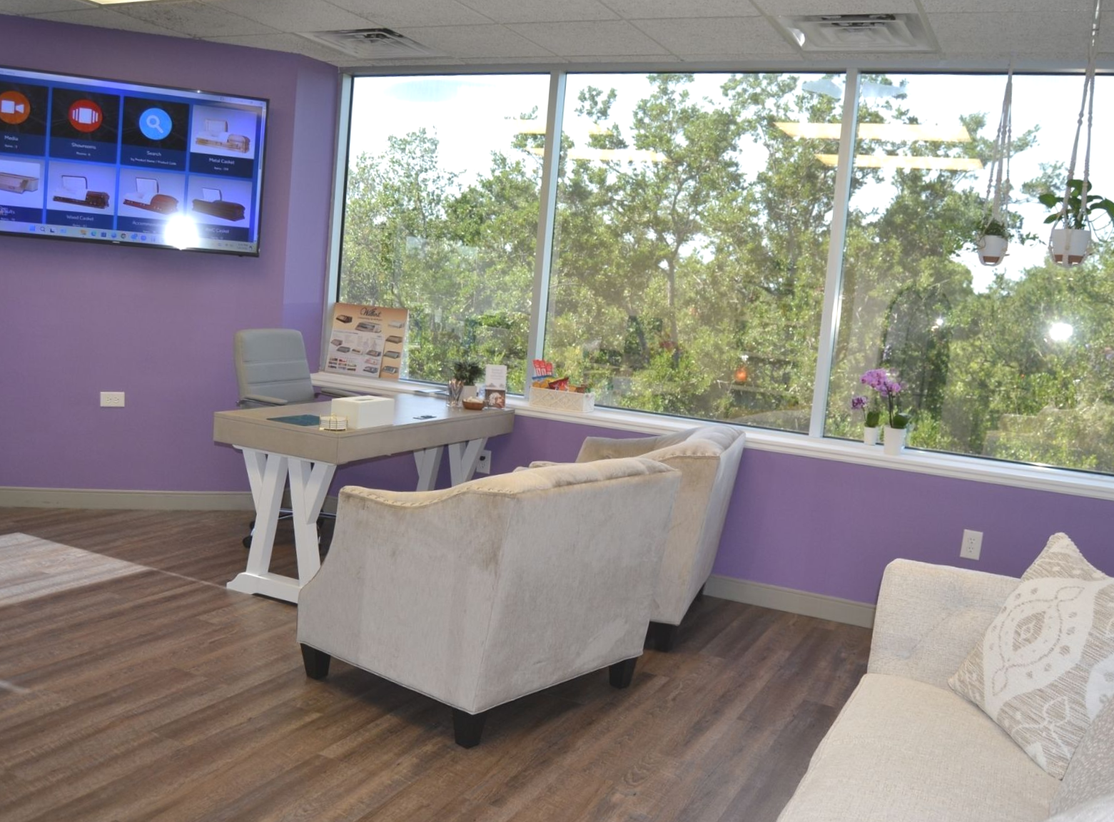 Purple waiting room with white chairs, wall TV, and large windows overlooking trees.