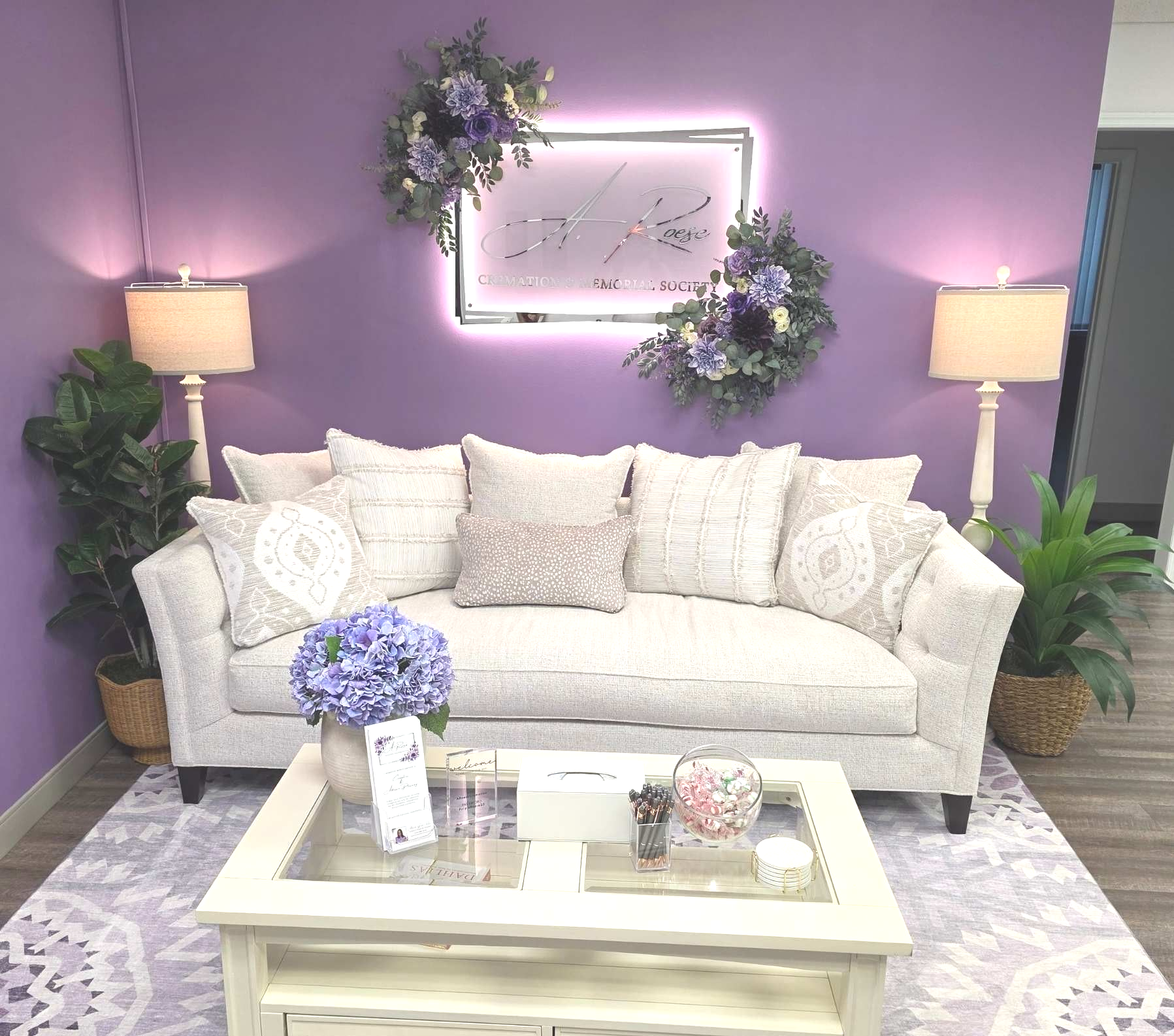 Lavender living room with a plush white sofa and pillows, a coffee table, and floral wall decor.