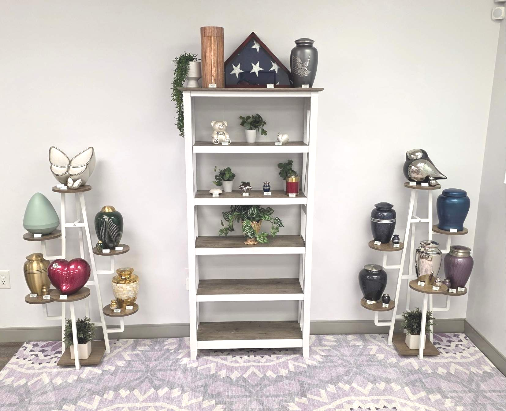 Decorative shelves with urns and keepsakes flanking a white ladder shelf on a light patterned purple themed rug.