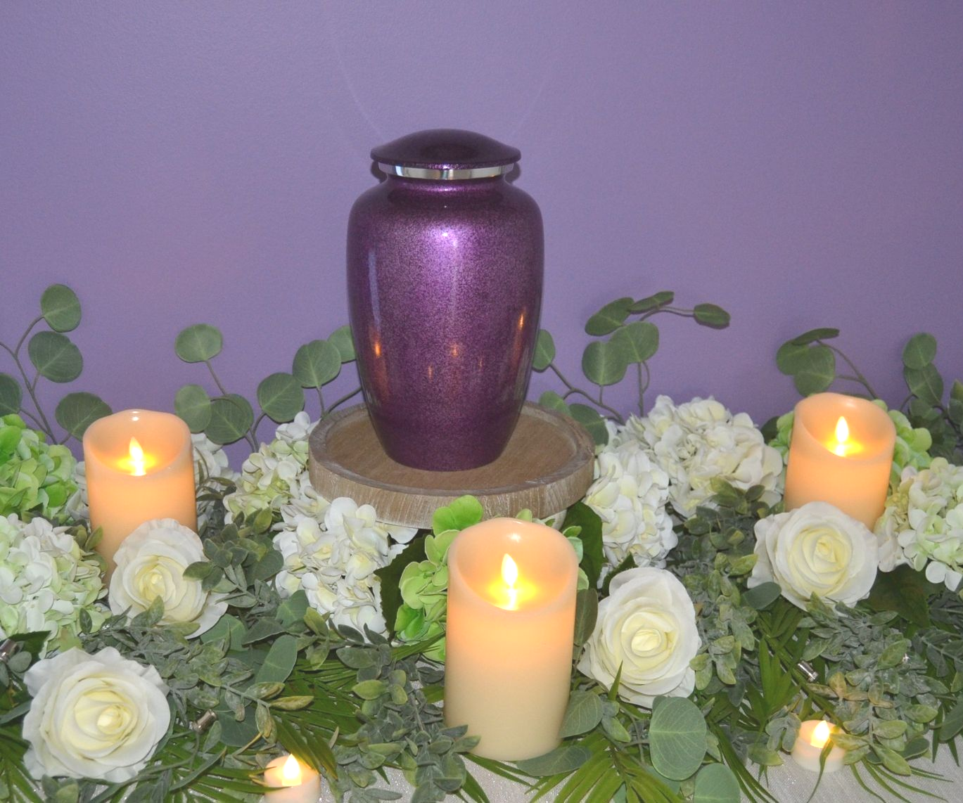 Purple urn surrounded by white roses and lit candles on a floral memorial display