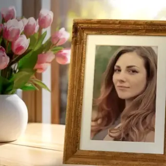 Framed portrait on a wooden table beside a white vase of pink tulips.