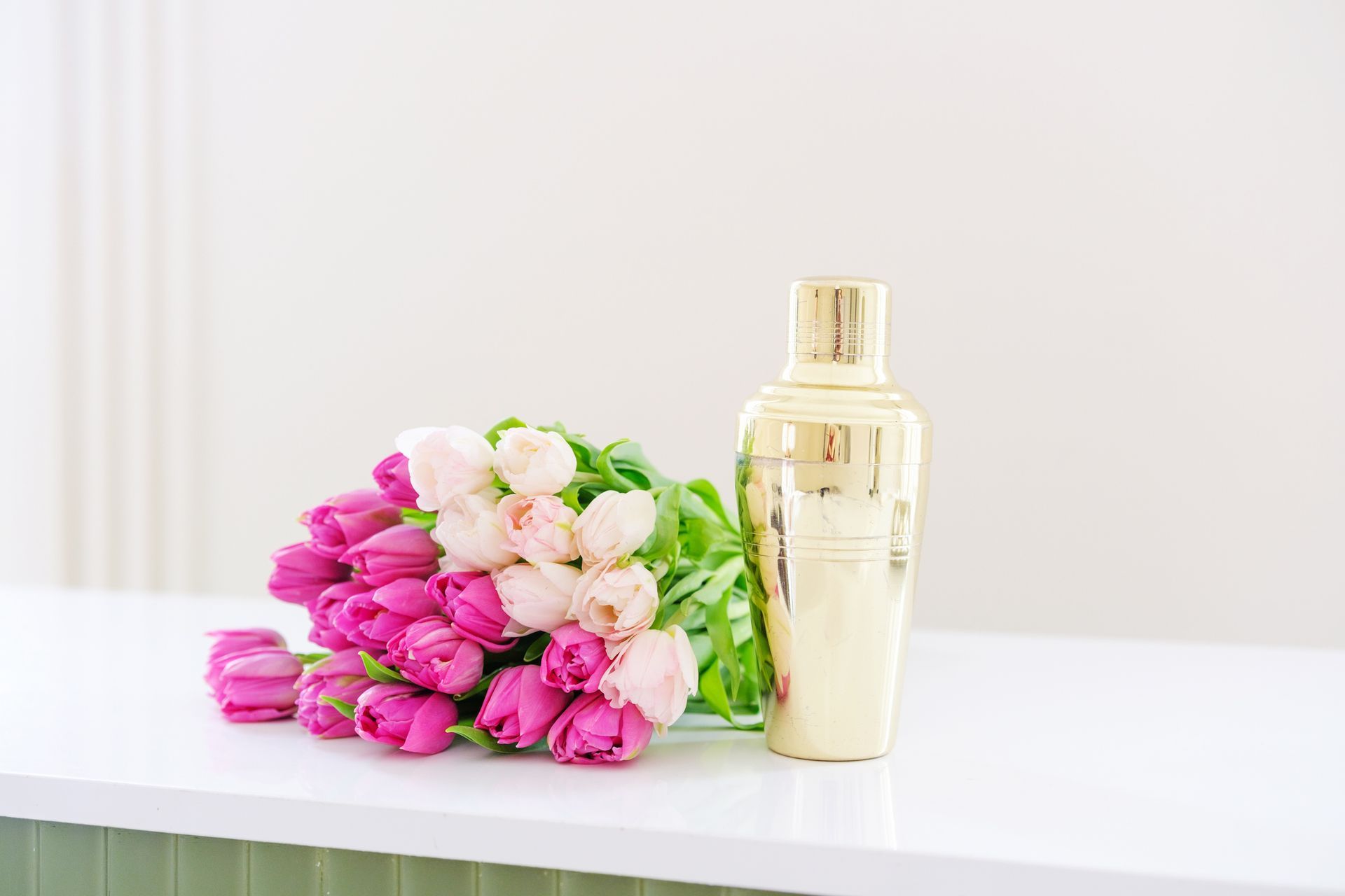 Pink and white tulips beside a gold perfume bottle on a white table