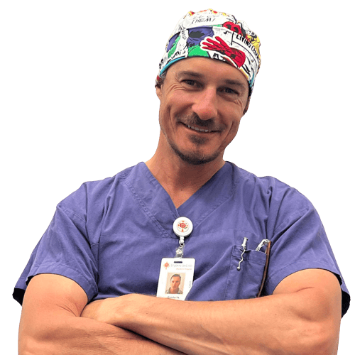 A man wearing a purple scrub top and a colorful hat is smiling with his arms crossed.