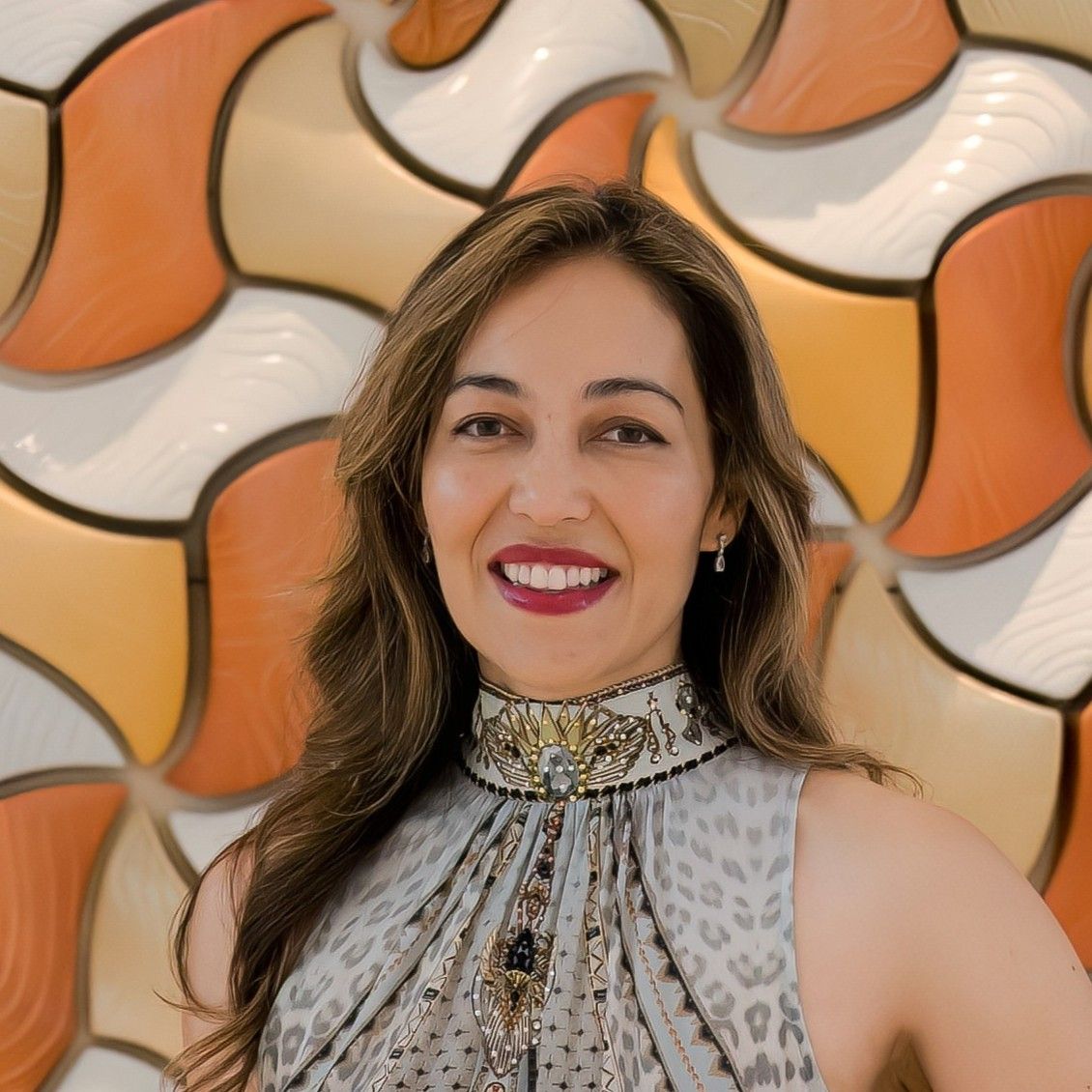 Aurora Bariatrics team member, Associate Professor Ruth Blackham
with long wavy hair, wearing a high-neck patterned dress with ornate detailing, smiling in front of a textured orange and cream tile wall