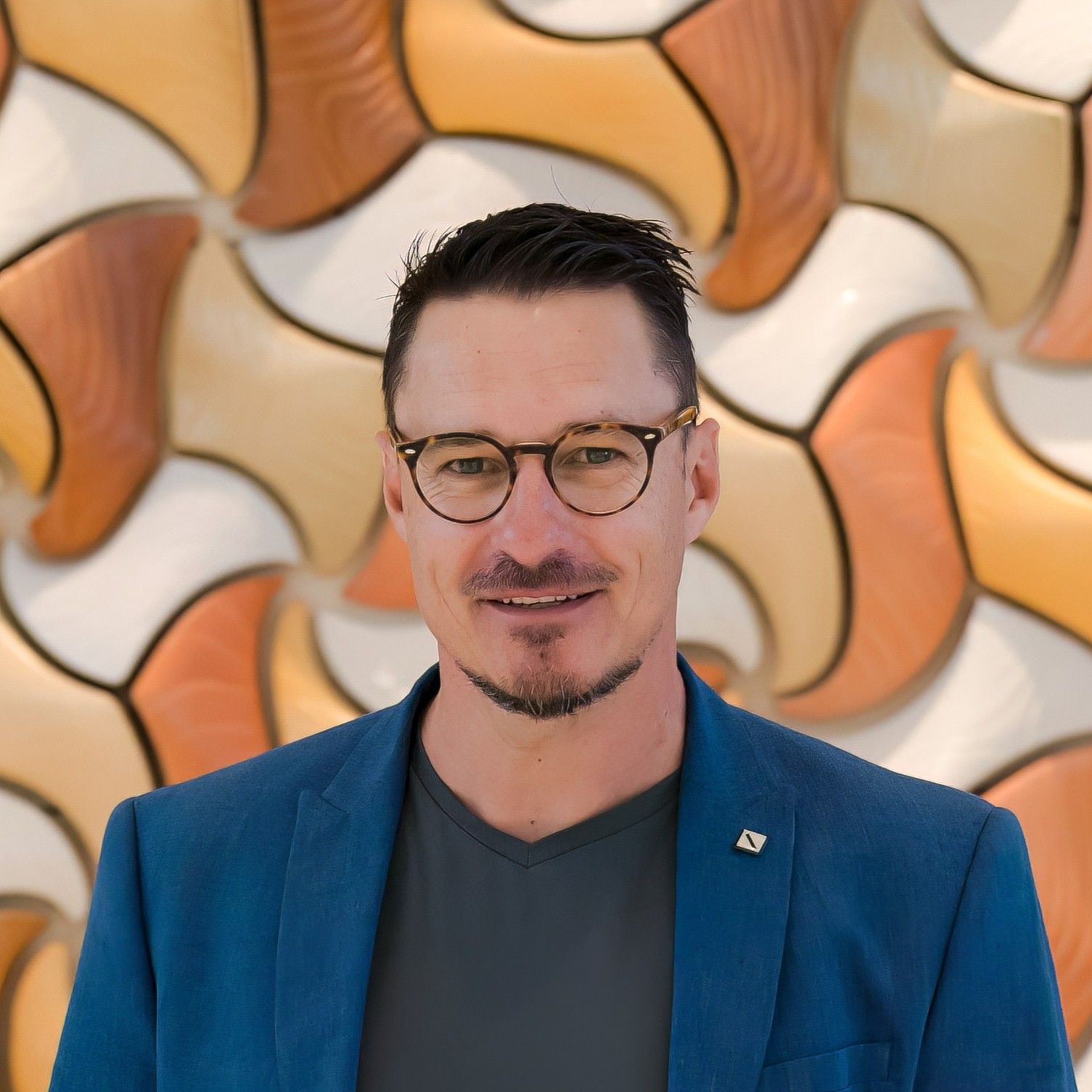 Aurora Bariatrics team member Frederik Myburgh wearing a blue blazer and glasses, smiling in front of a patterned orange and cream wall