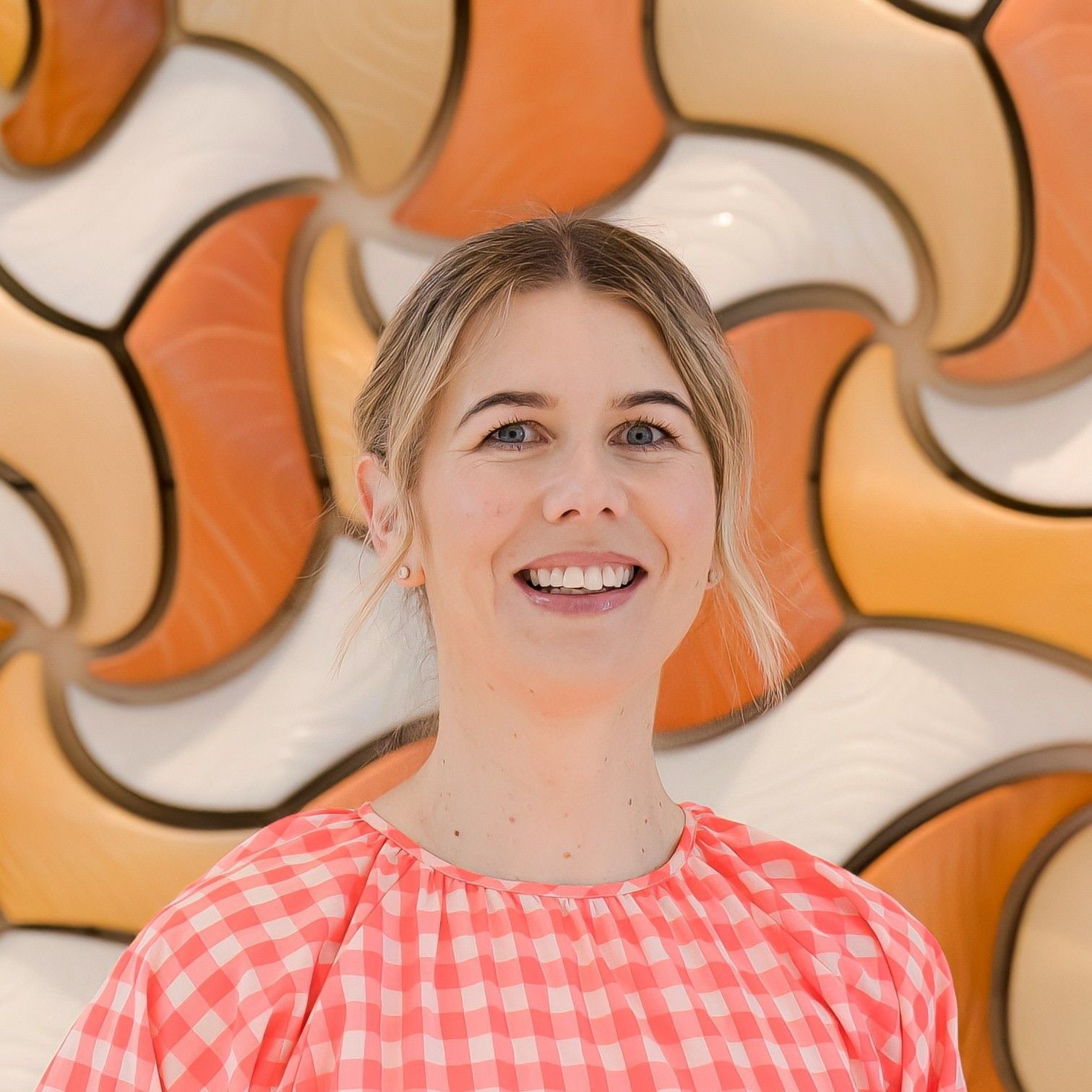 Aurora Bariatrics team member Dr Sigrid Uhlrich with blonde hair wearing a pink gingham blouse, smiling in front of a patterned orange and cream background