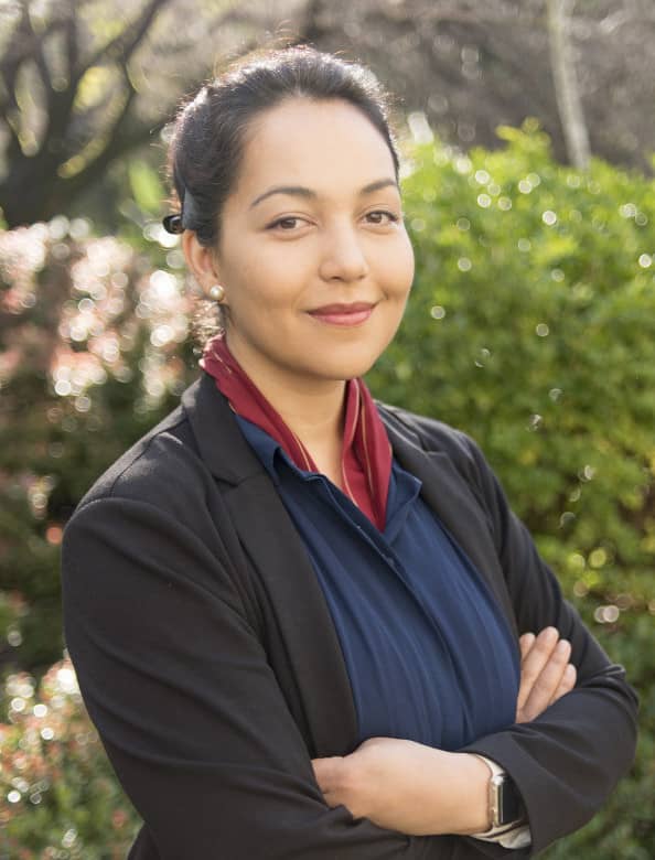 A woman in a black jacket and blue shirt is posing for a picture with her arms crossed.