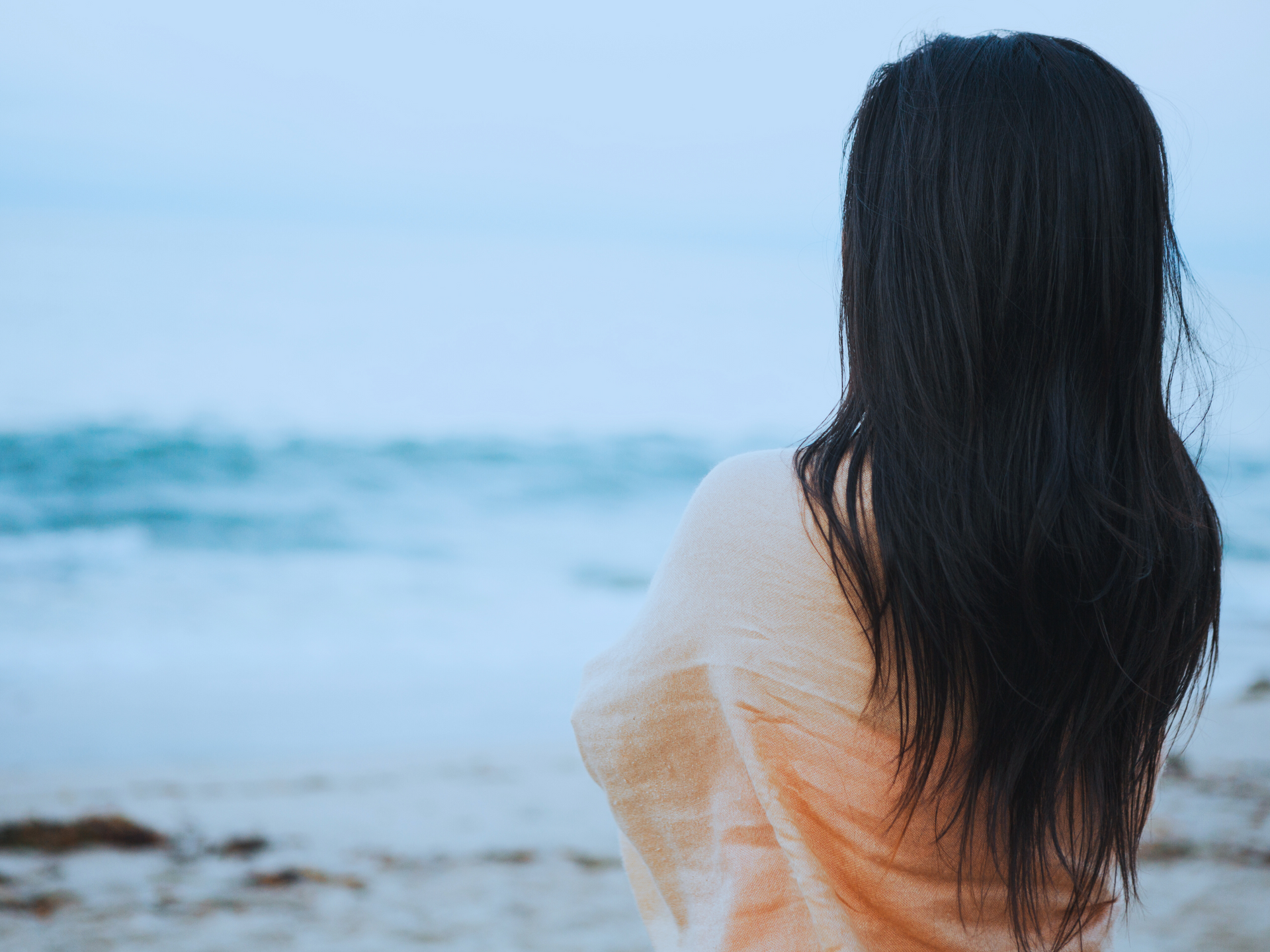 A woman is standing at the ocean on a cloudy day looking out.