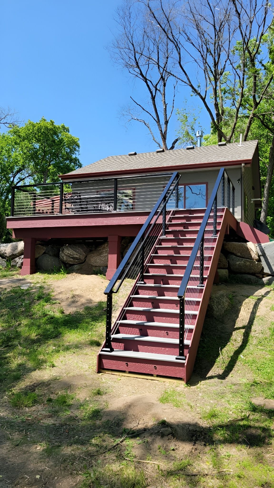 Cottage with a red deck and stairs leading up. The house is gray with a dark roof.