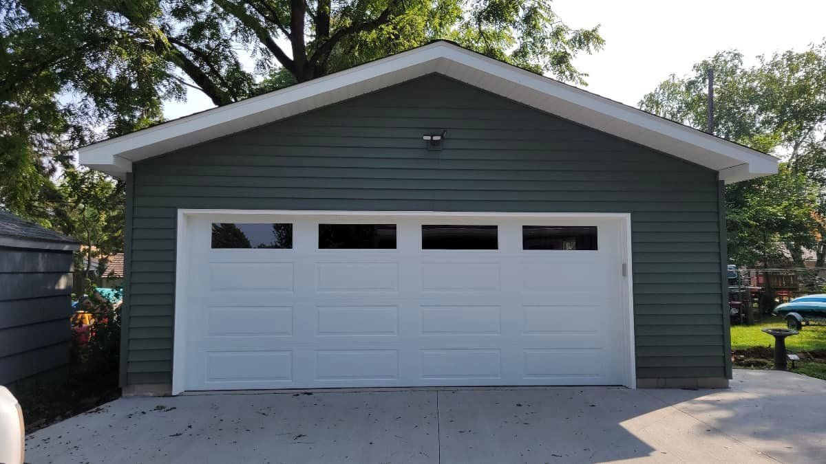 Green-sided garage with white door and roof trim against a backdrop of trees.
