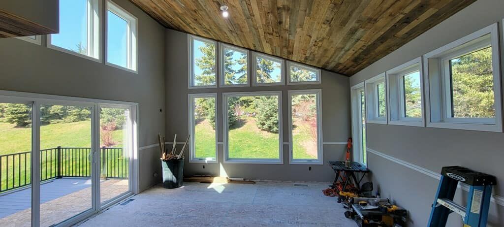 Interior room with large windows, wood ceiling, and unfinished flooring. Overlooks a green landscape.