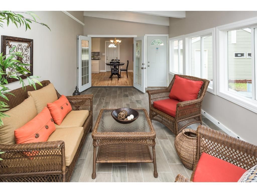 Sunroom with brown wicker furniture and red cushions. Opens to a dining area.