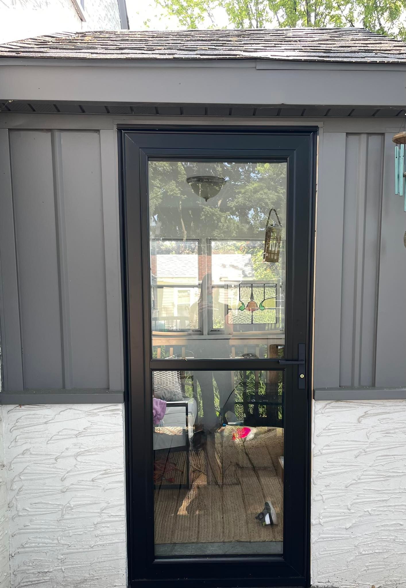 Black-framed screen door on a grey shed; trees reflected in the glass.