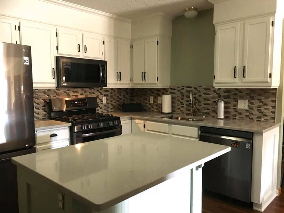 Kitchen with white cabinets, stainless steel appliances, mosaic tile backsplash, and an island.
