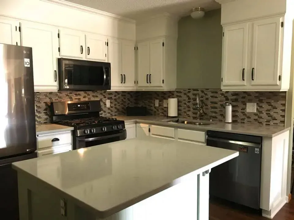 White kitchen with island, stainless steel appliances, and patterned tile backsplash.