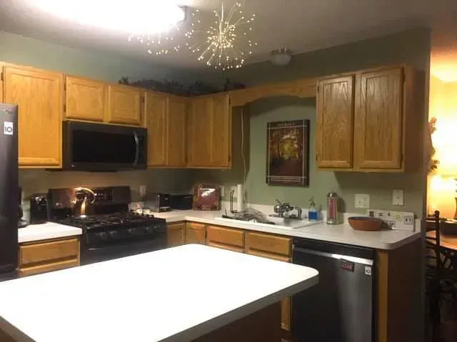 Kitchen with light brown cabinets, black appliances, white countertops, and a white island.
