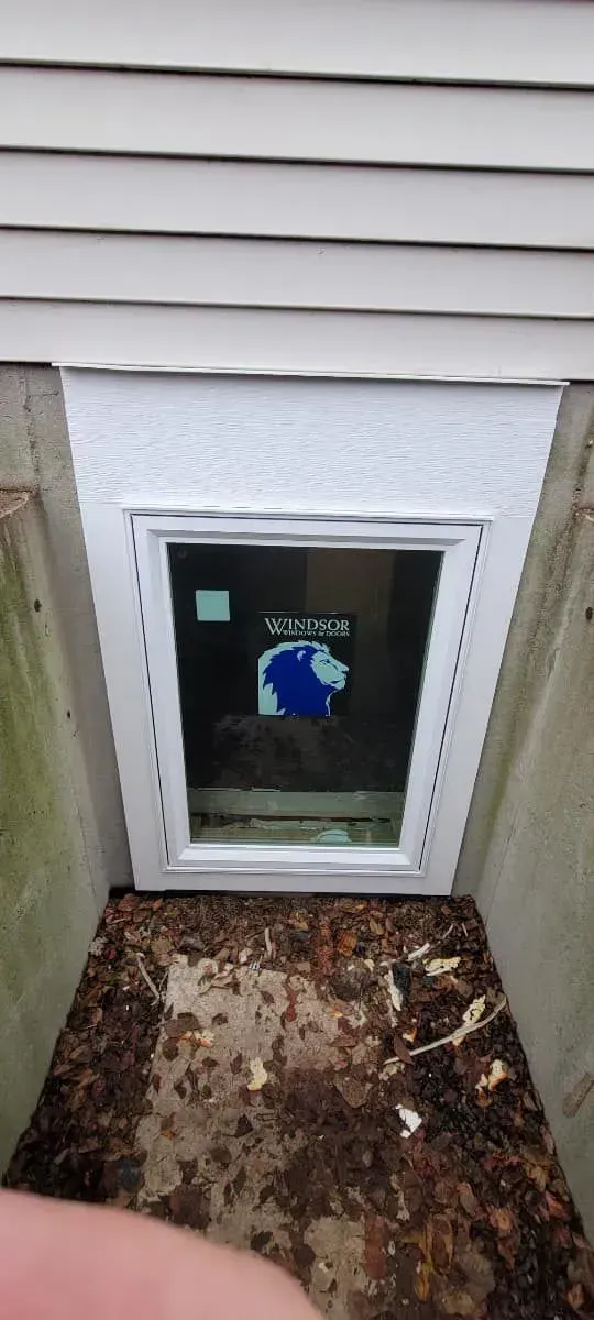 Basement window in a window well, surrounded by siding and debris.