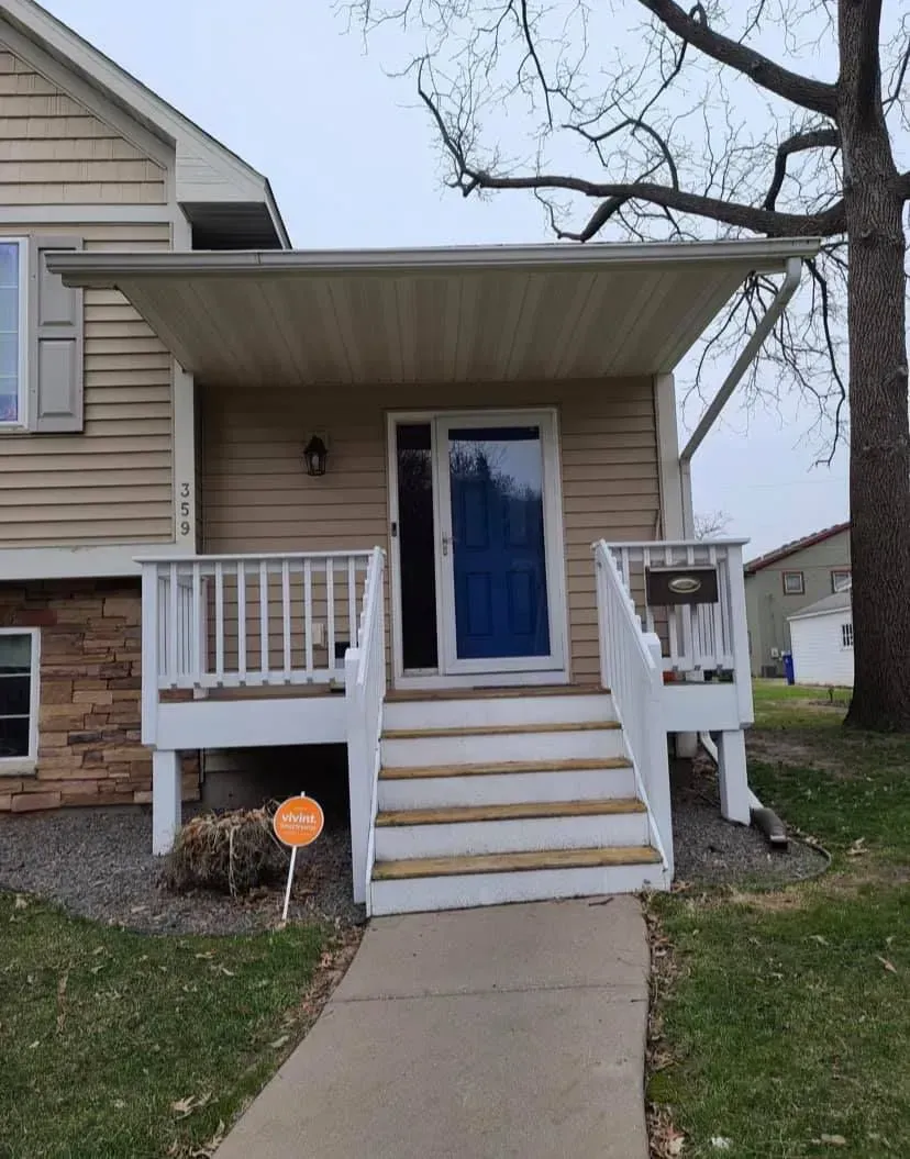 House entrance with porch, stairs, blue door, and covered overhang.