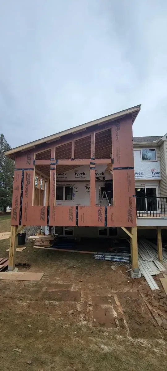 Exterior of a house addition under construction with a slanted roof and exposed framing on a cloudy day.