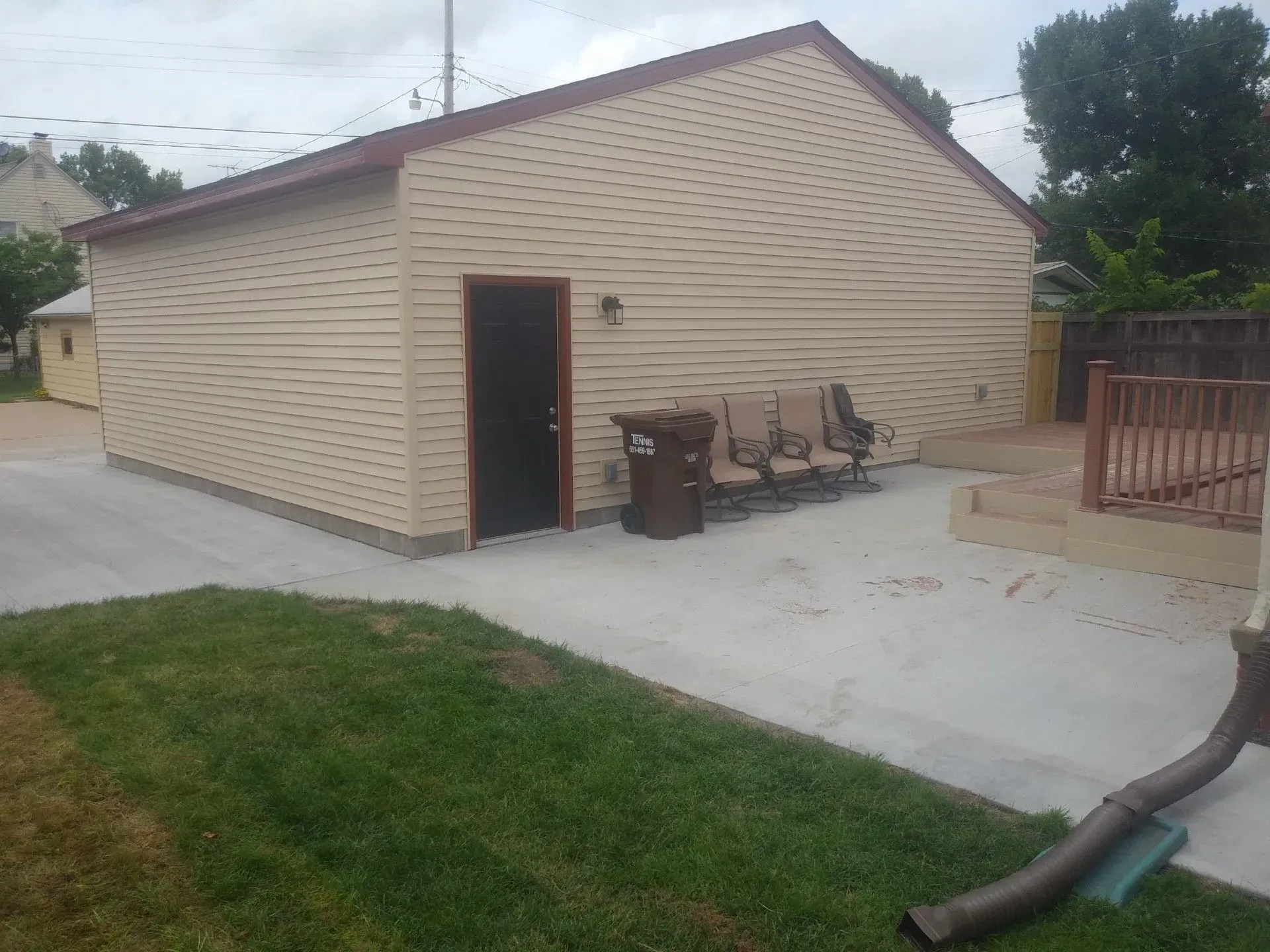 Tan building with a black door, chairs, and a brown trash can. 