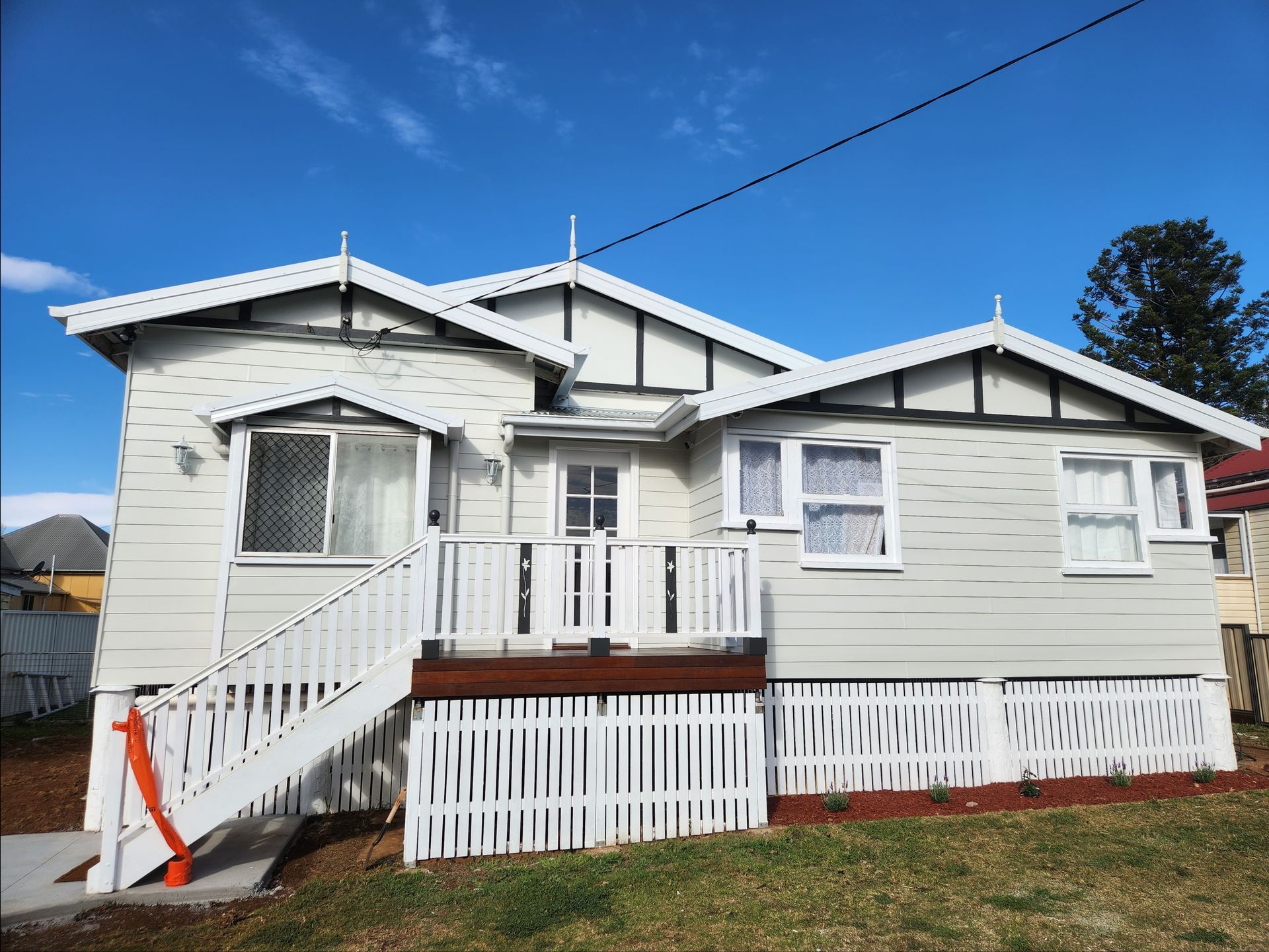 A light-colored house with white trim and a small porch. A clear blue sky is visible.