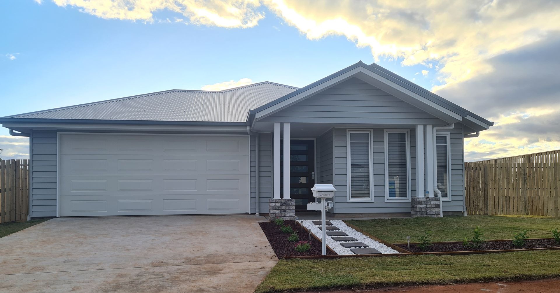 Gray house with attached garage, small front yard, and wooden fence against a cloudy sky.