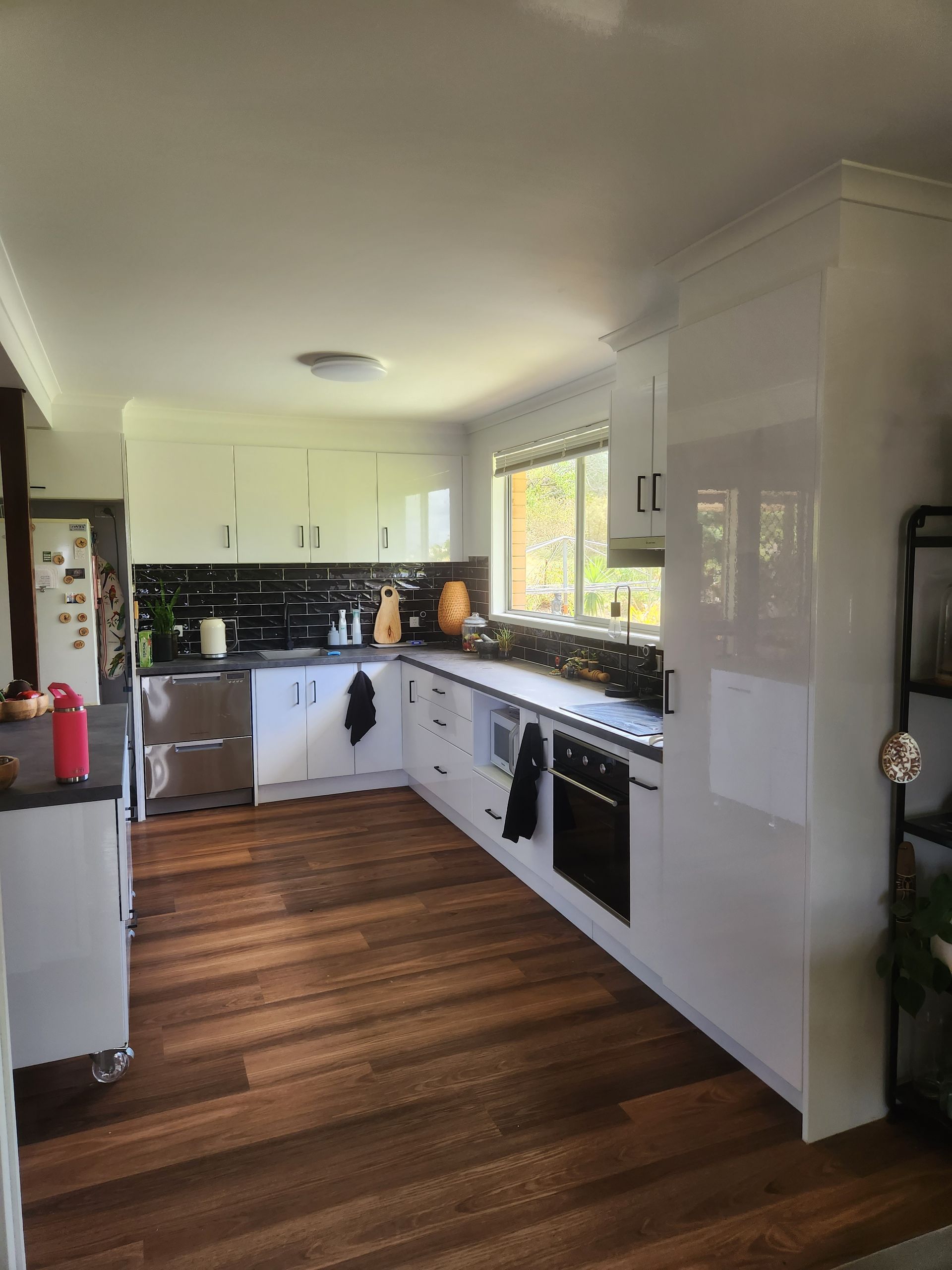 Kitchen with white cabinets, black backsplash, stainless steel appliances, and wood floor.