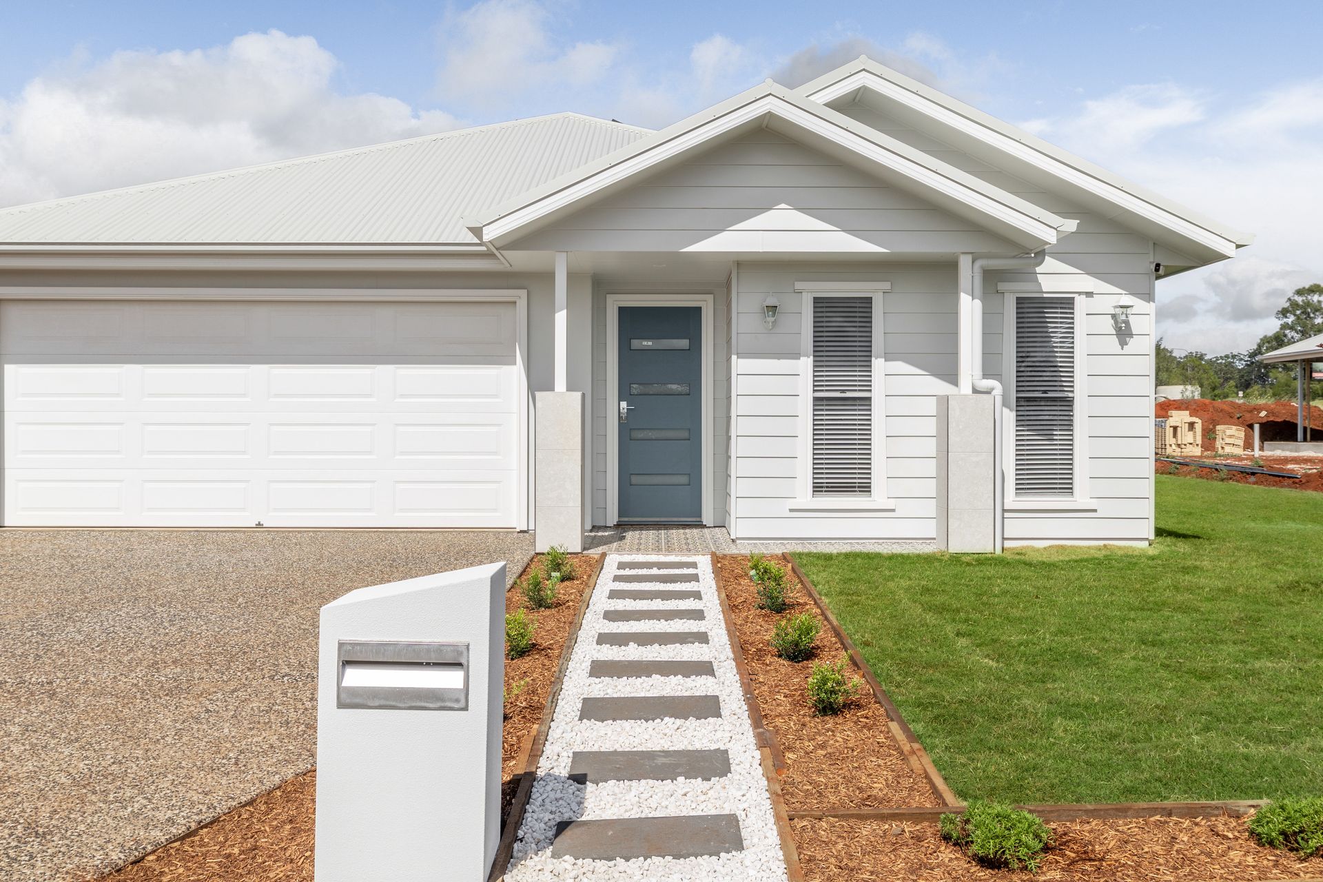 White house with a garage, blue door, and a pathway leading to the entrance.