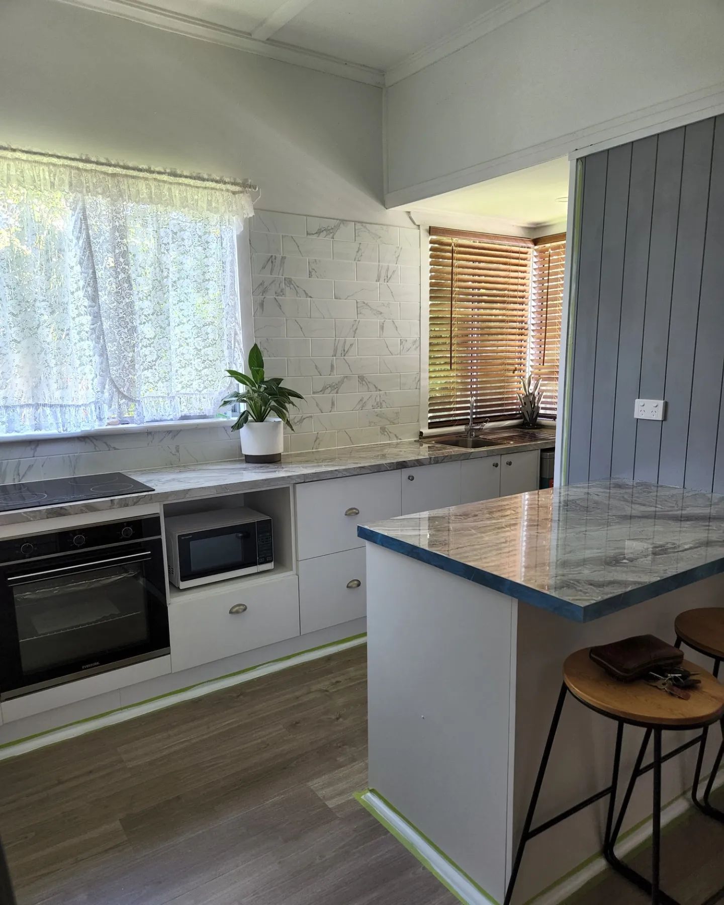 Kitchen with white cabinets, marble backsplash, island with stools, and window with blinds.