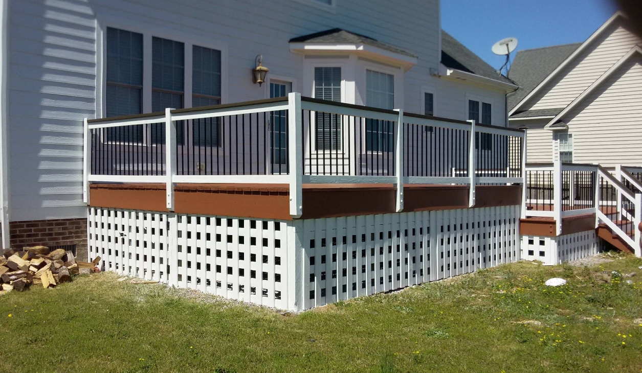 A multi-level white deck with brown lattice skirting, attached to a white house with black railing, in a grassy yard.