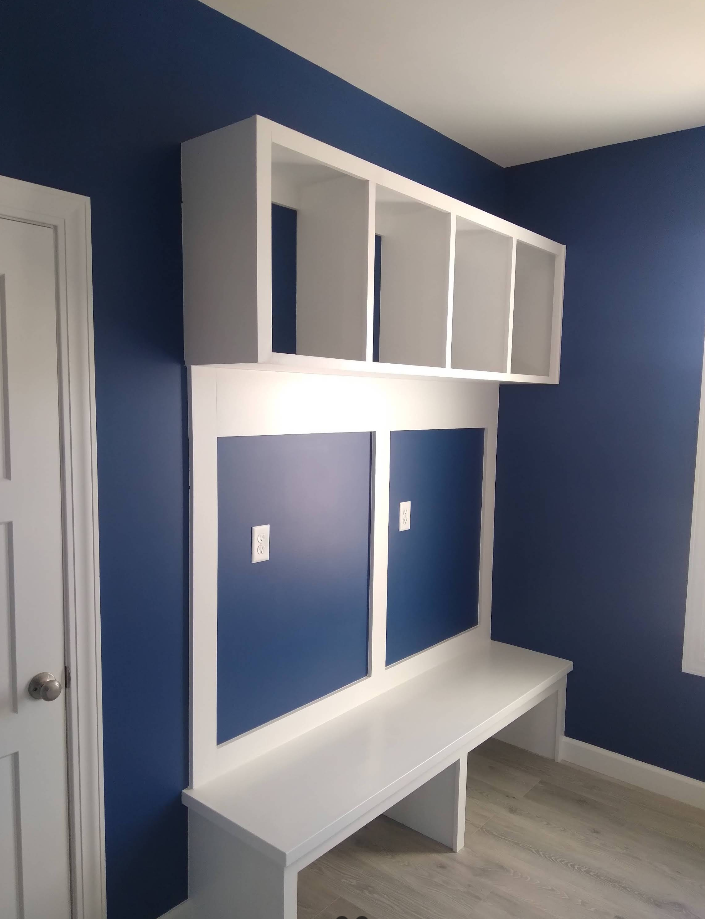 Built-in white desk and shelving unit on a blue wall. It features a desk with shelving above.