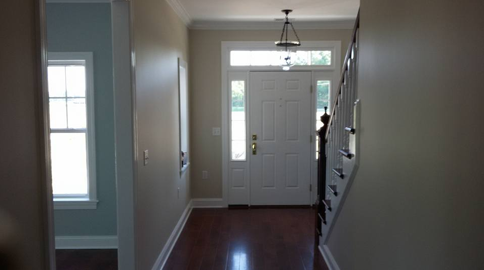 Entryway with a white door, wood floors, and a staircase on the right. Beige walls and trim throughout.