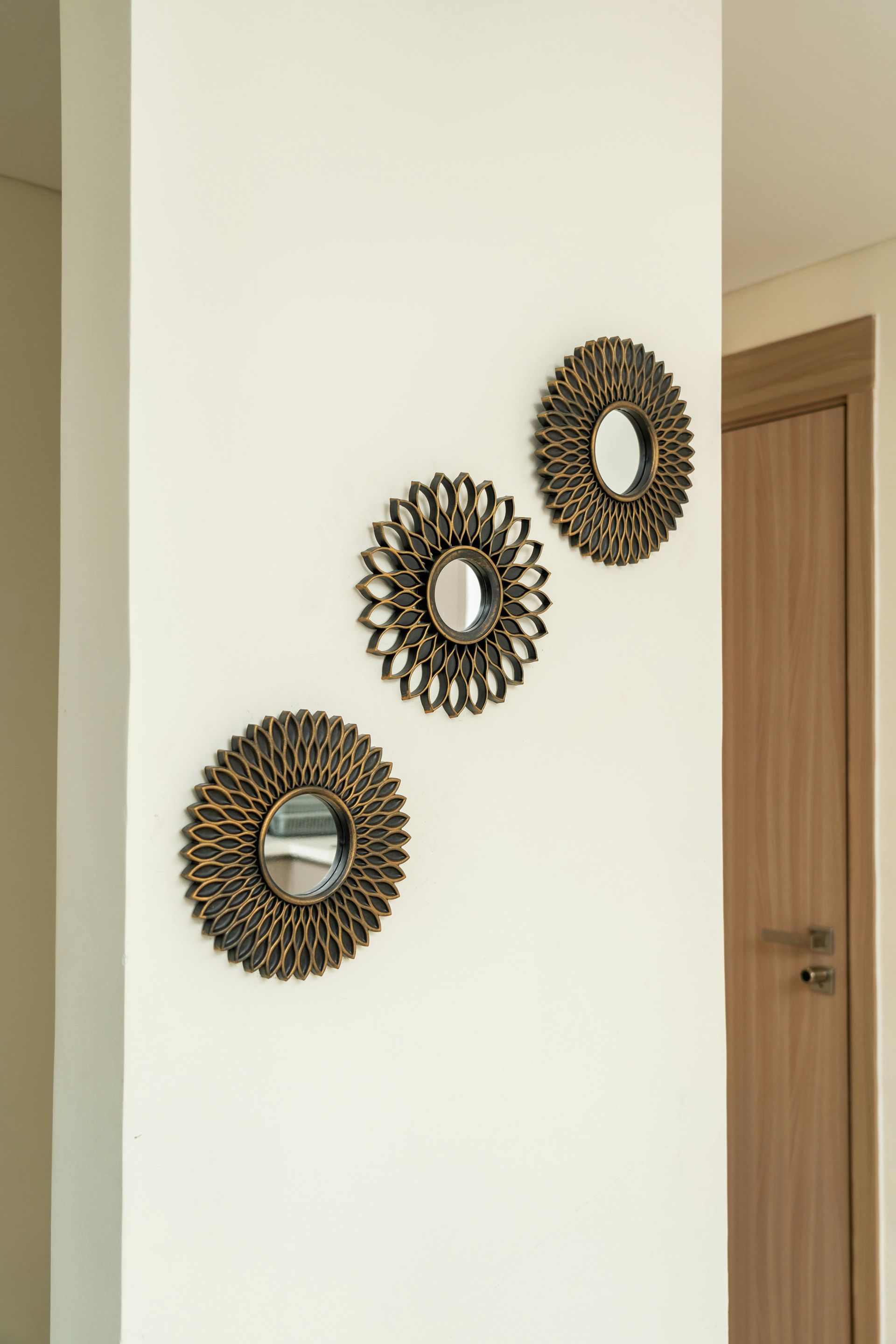 Three woven wall mirrors arranged diagonally on a white wall beside a wooden door.