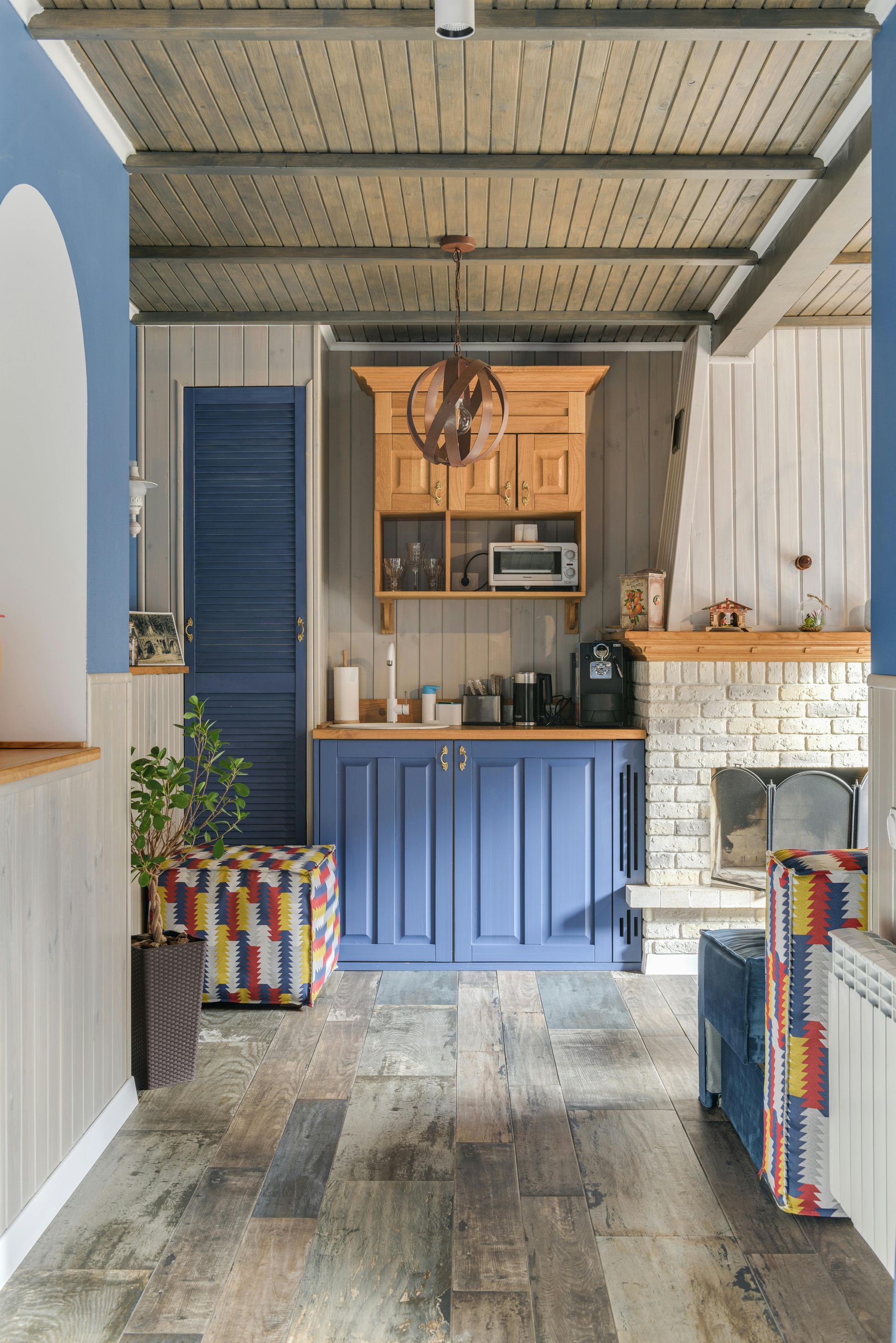 A narrow kitchen with blue and wood cabinets, a microwave, and a fireplace. The walls are white and wood.