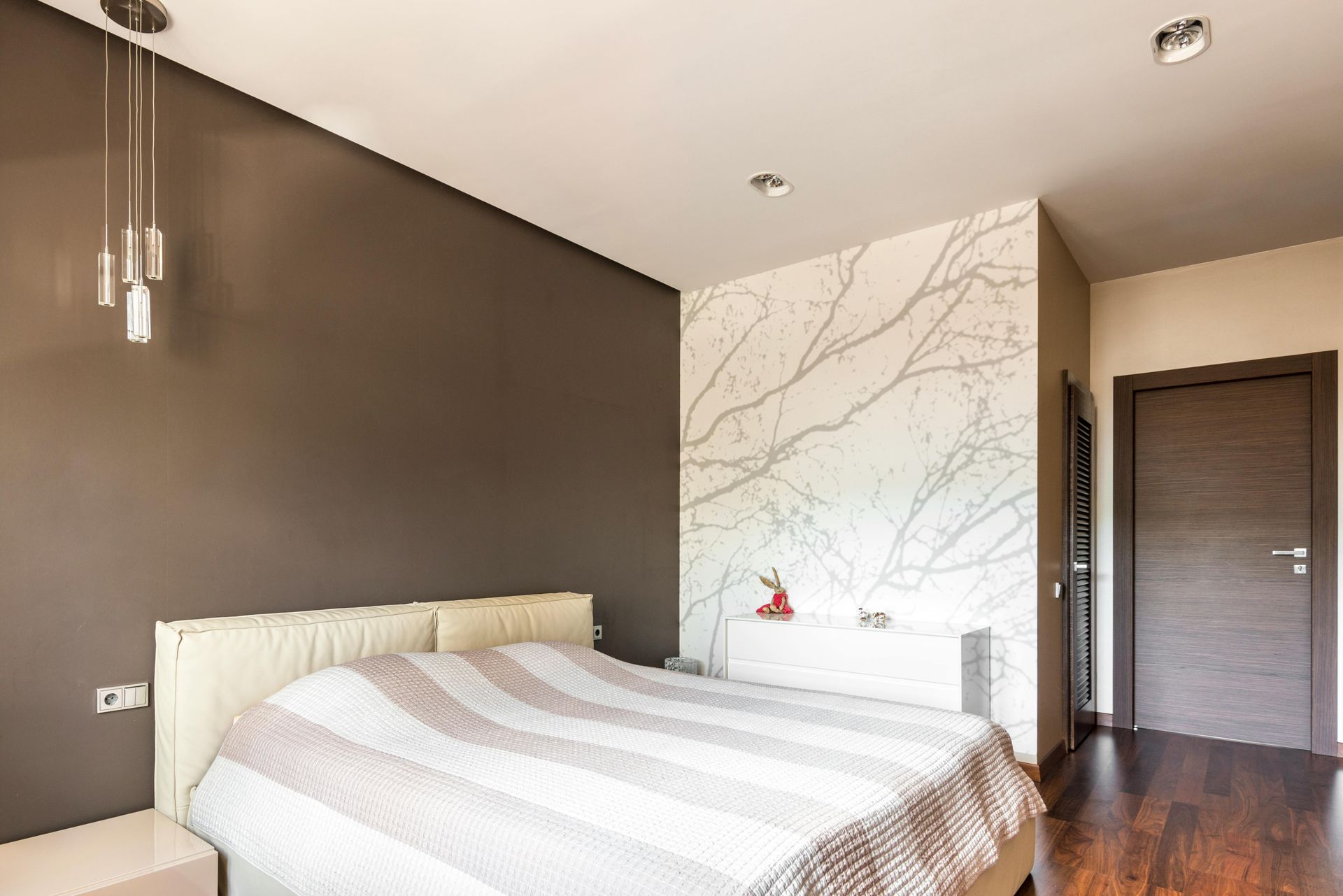 Bedroom with brown and white walls, bed with striped blanket, and pendant lights.