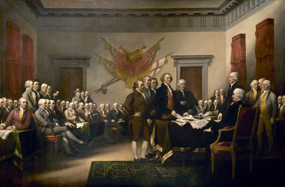 Men gathered around a table in a historic chamber, with a large eagle emblem on the back wall.