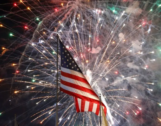 An American flag stands in front of a fireworks display.