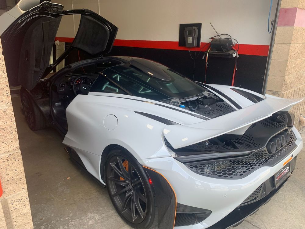 White McLaren sports car with open doors, black stripes, and orange accents in garage.