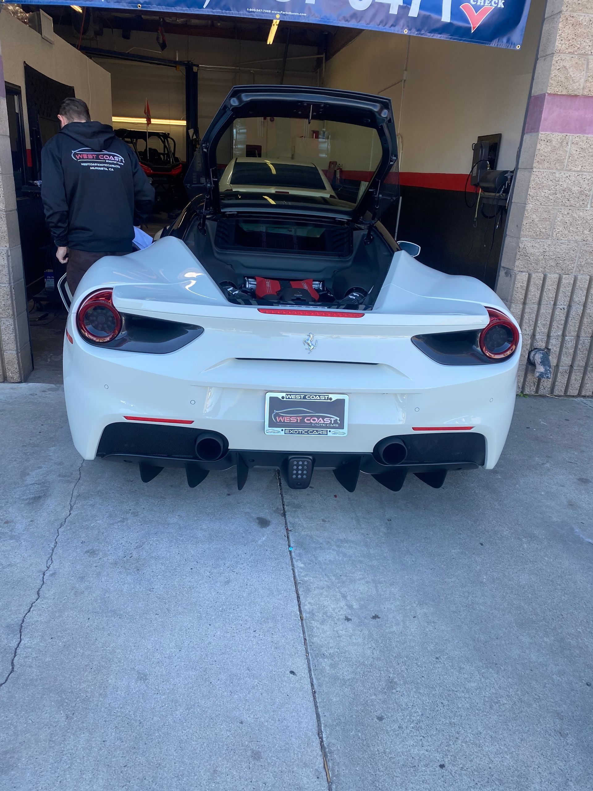 White Ferrari convertible with open trunk inside a garage; person in the background.