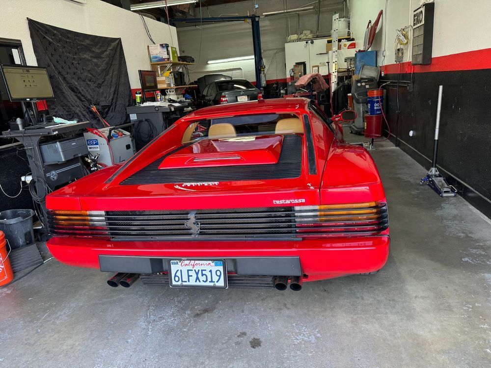 Red Ferrari Testarossa sports car in a garage with California license plate.