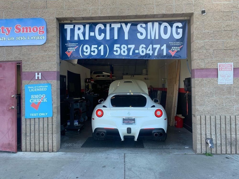 White Ferrari inside Tri-City Smog station, with a sign for smog checks.