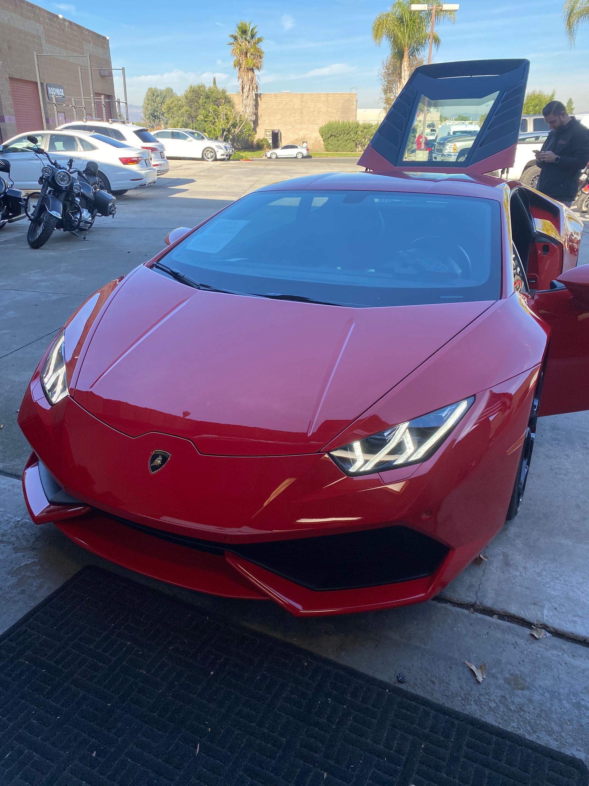 Red Lamborghini with doors open, parked outdoors on a sunny day.