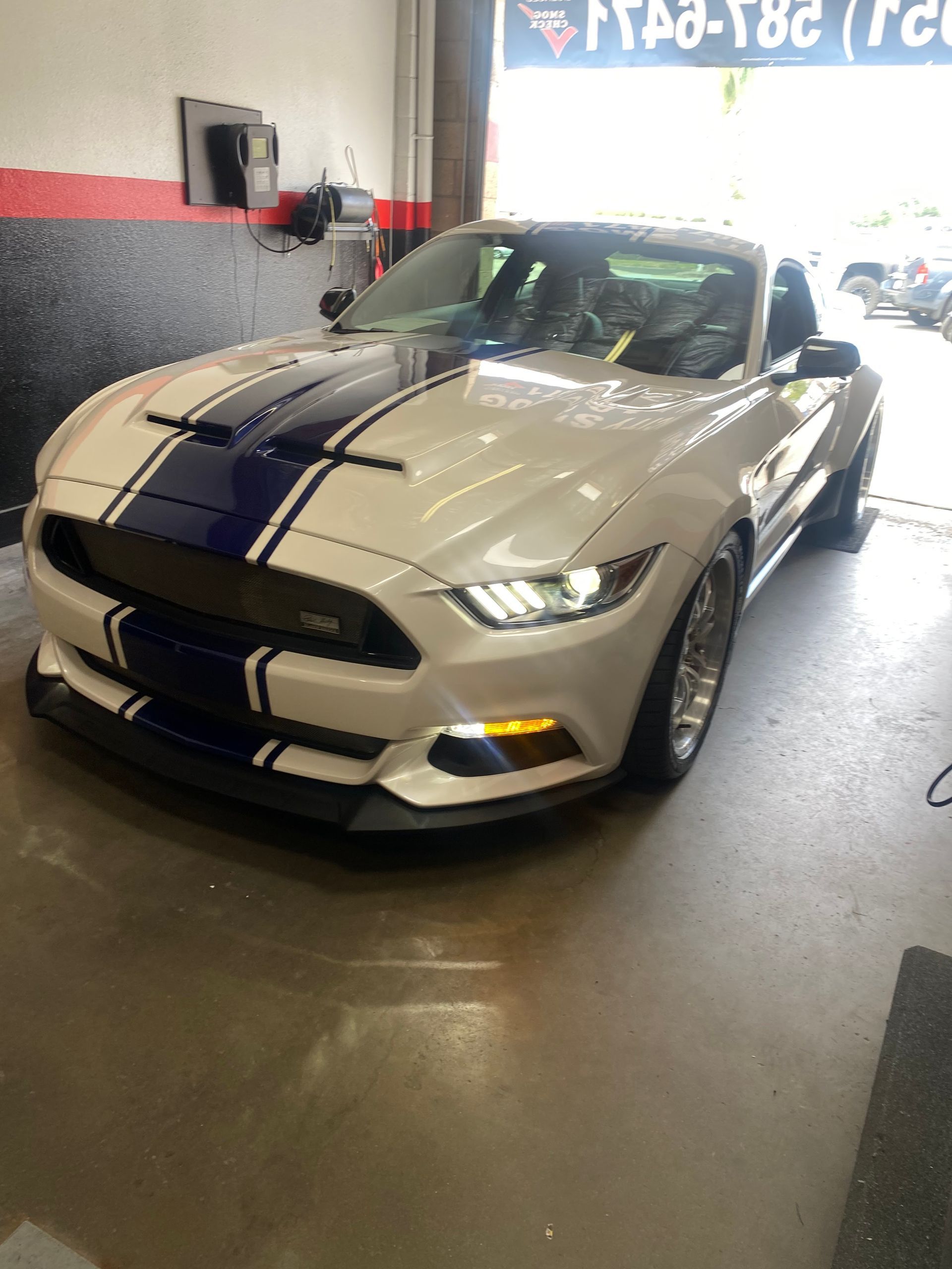 White Ford Mustang with blue racing stripes, parked in a garage.