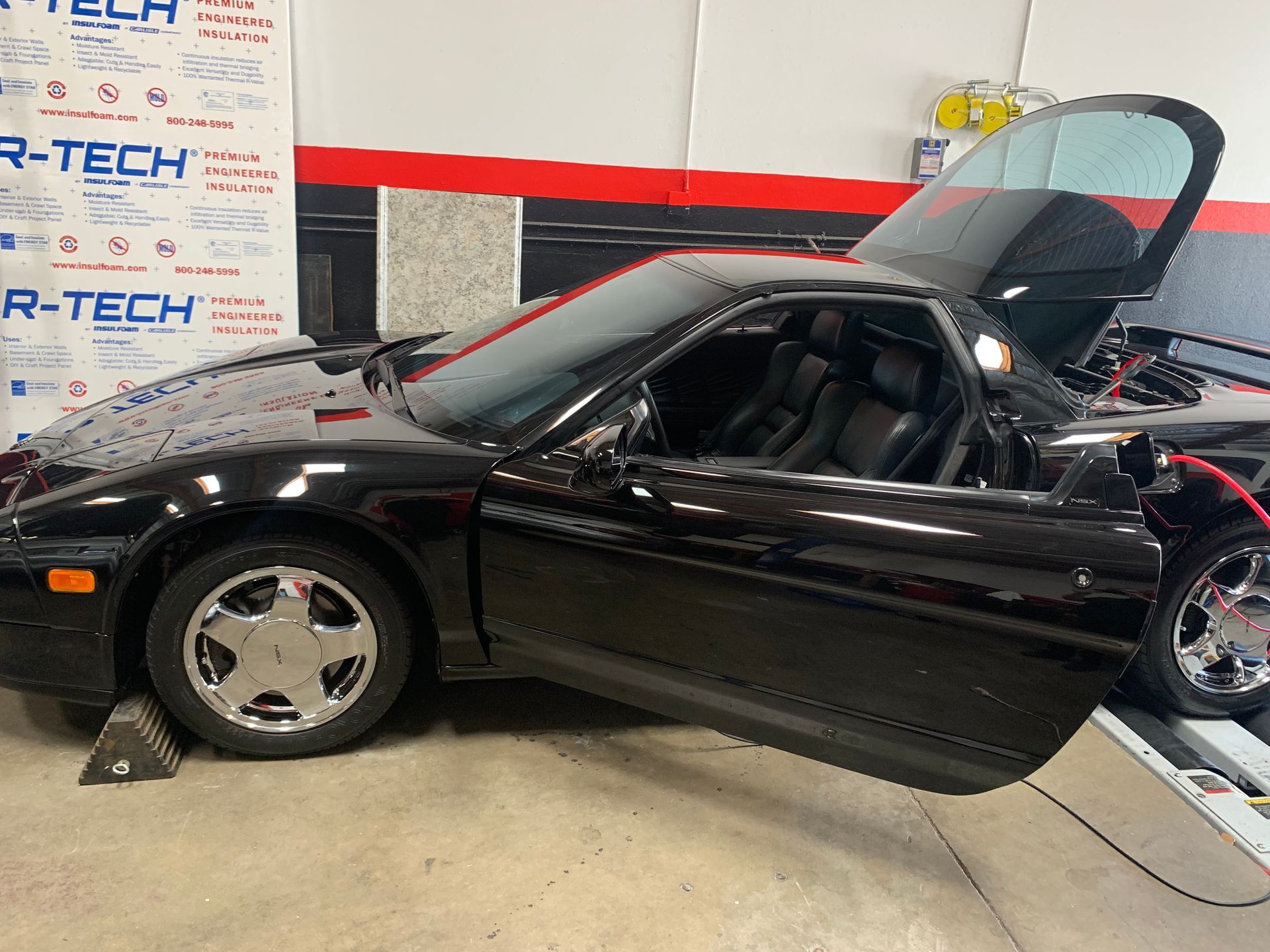 Black Honda NSX sports car, doors and hood open, on a lift in a garage.