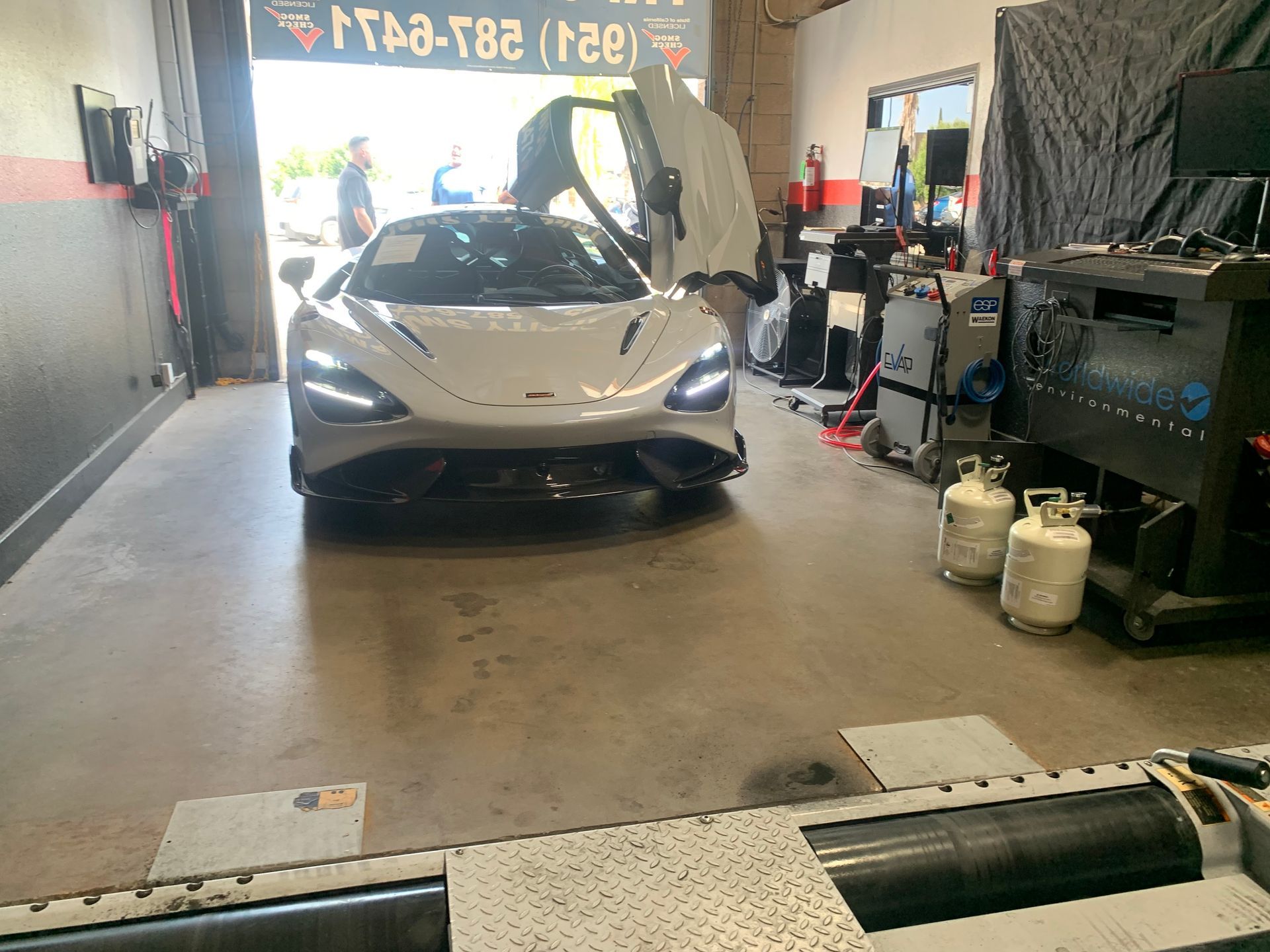 White McLaren sports car inside a garage, doors open.