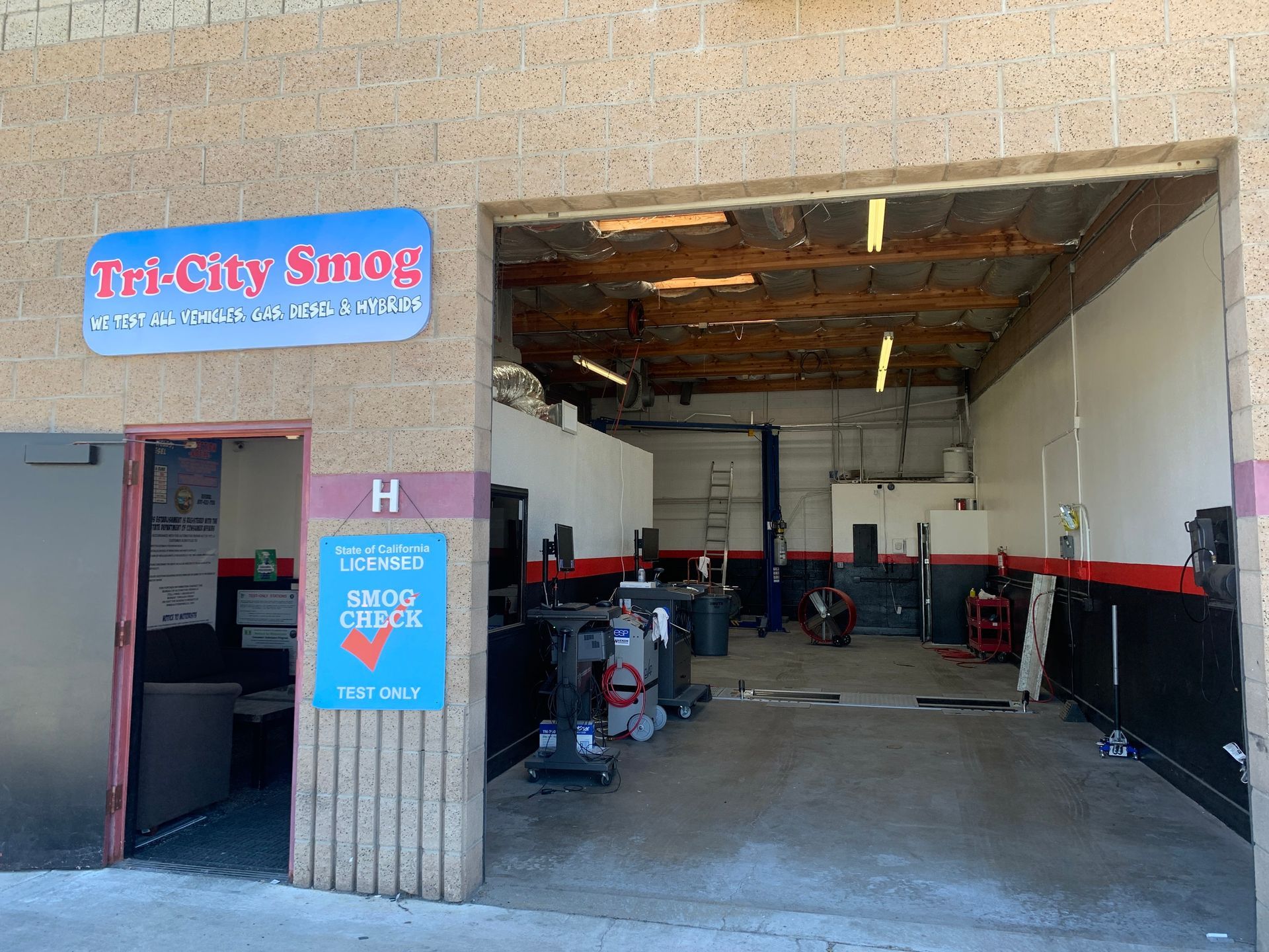 Tri-City Smog shop entrance. Sign above, open bay, equipment inside. Blue and red accents.