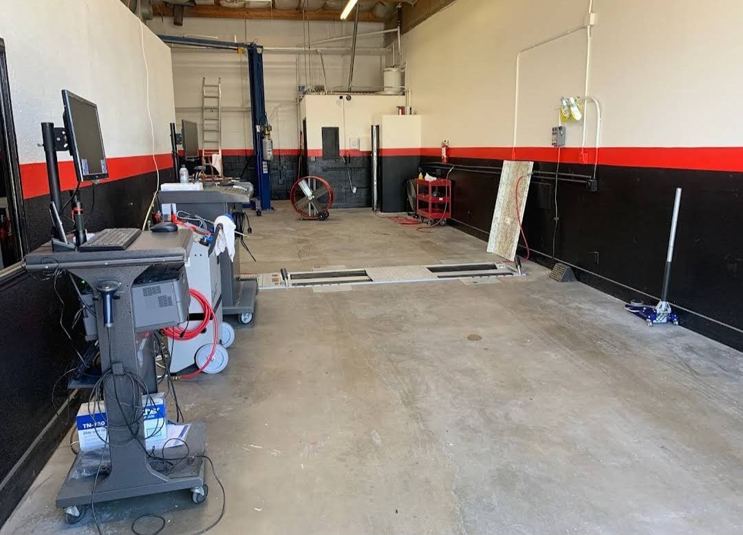 Car repair shop interior with alignment machine, lift, and tools on the floor; red and black accent wall.