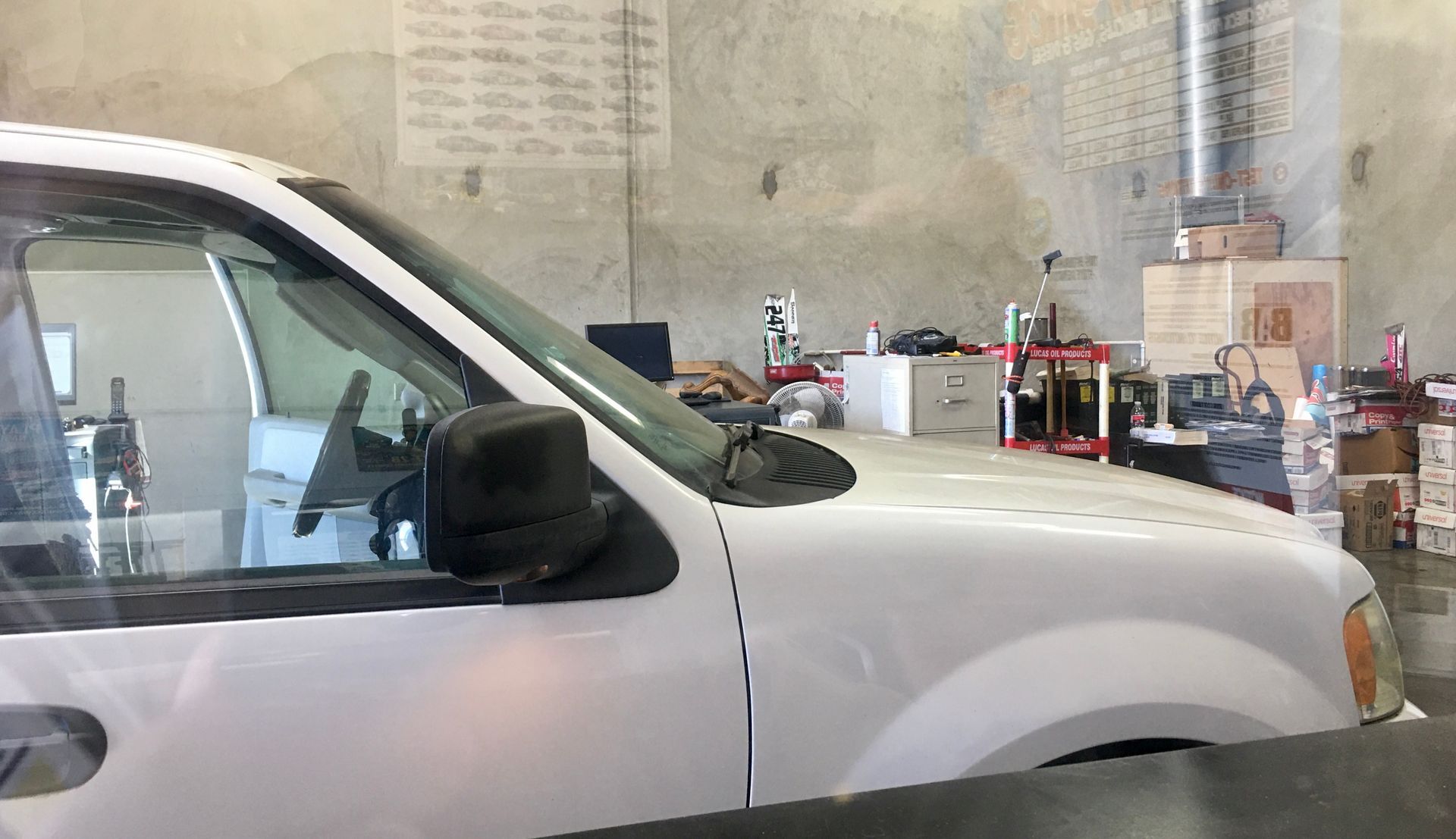White car in a cluttered garage, with a desk and various items in the background.