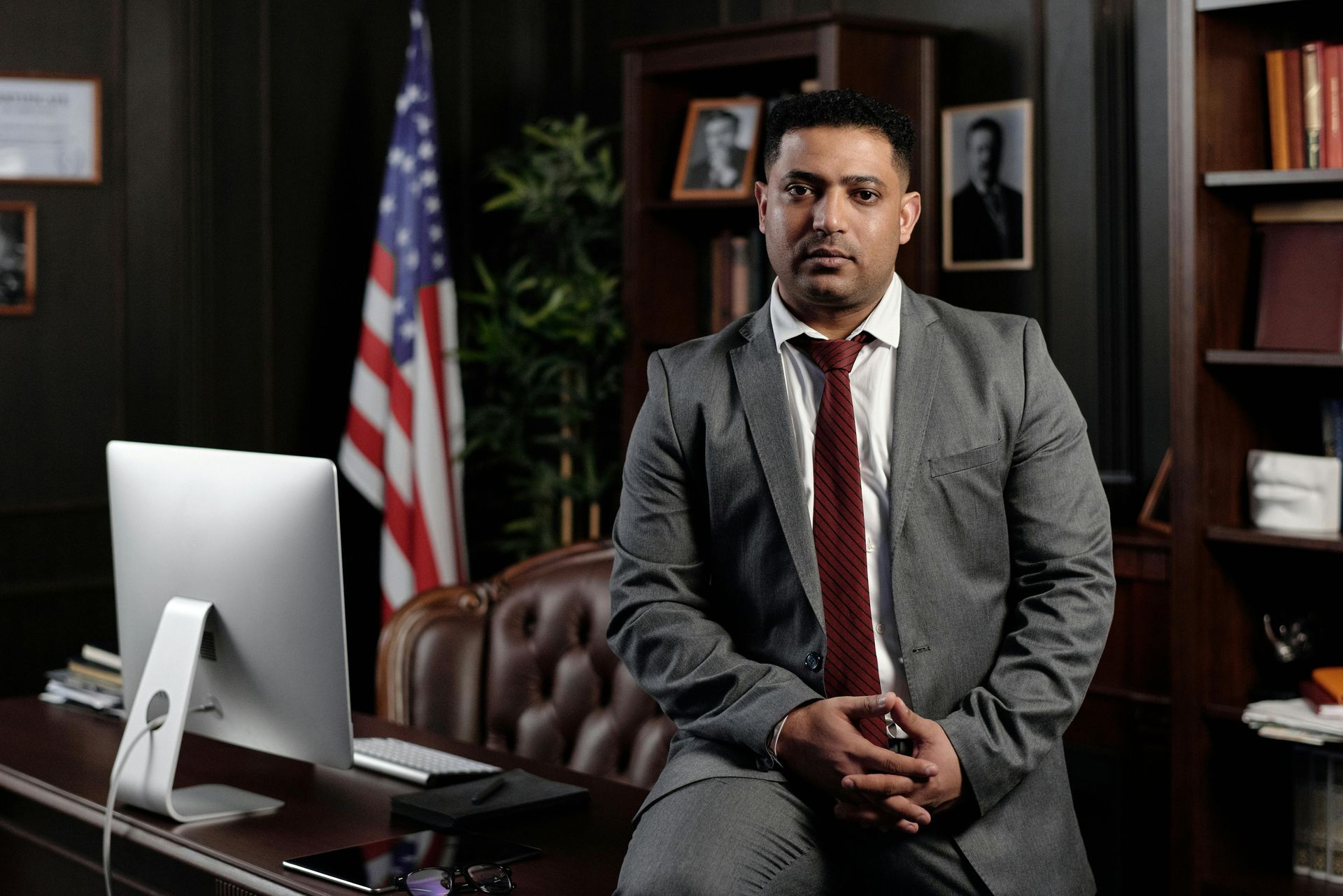 An attorney  in a suit and tie is sitting at a desk in front of a computer.