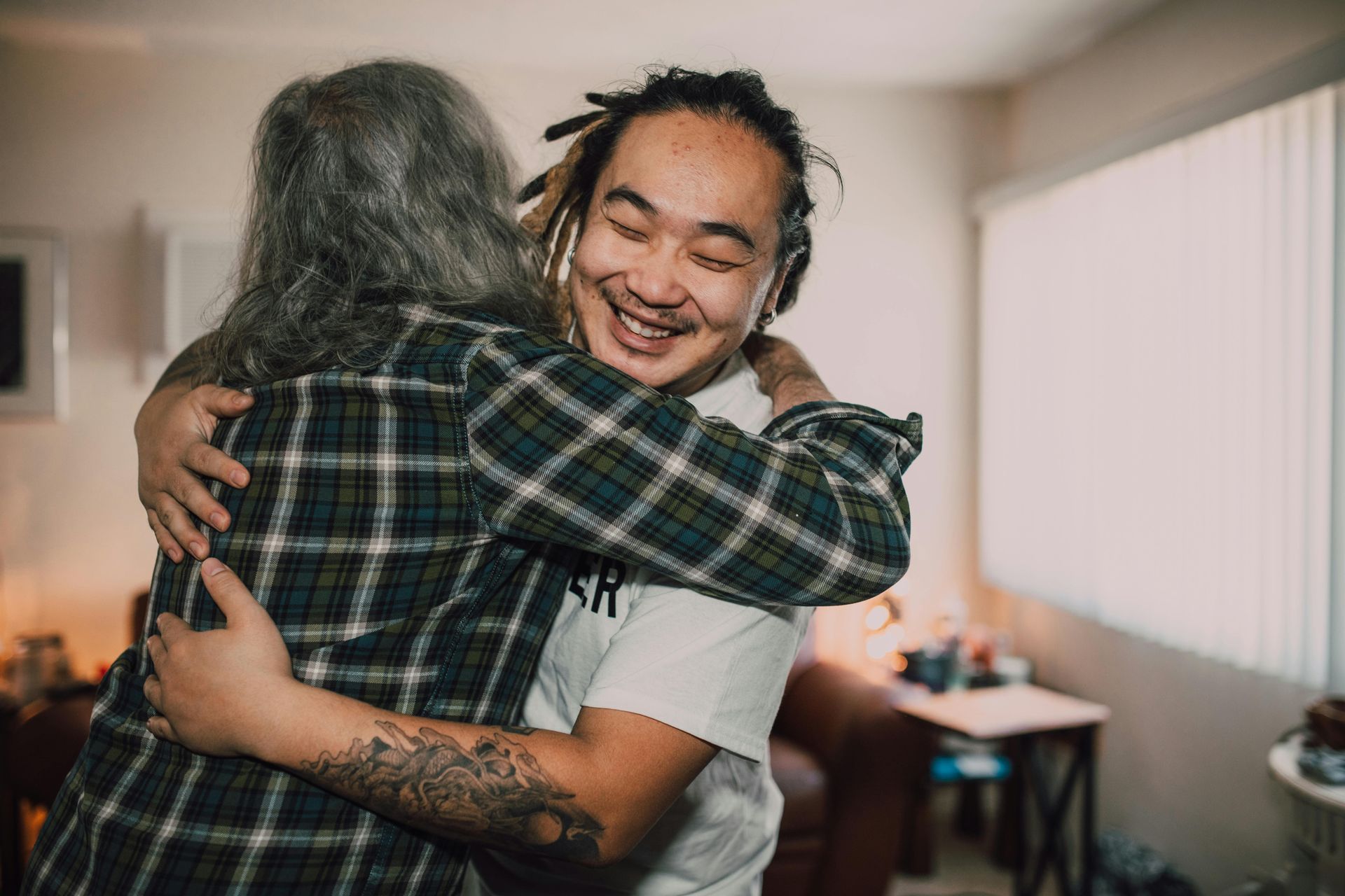 A young man is hugging an older women in a living room.